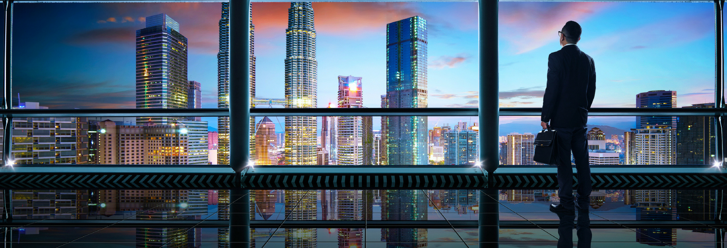 An image of a man in a high rise building look out over the city horizon.